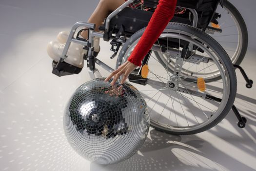 Woman in wheelchair reaches towards a sparkling disco ball, symbolizing empowerment and creativity.