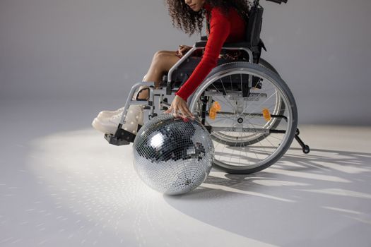 A woman in a wheelchair interacting with a disco ball on a white background.