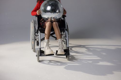 Free A person in a wheelchair holding a disco ball, showcasing trendy and fashionable style. Stock Photo