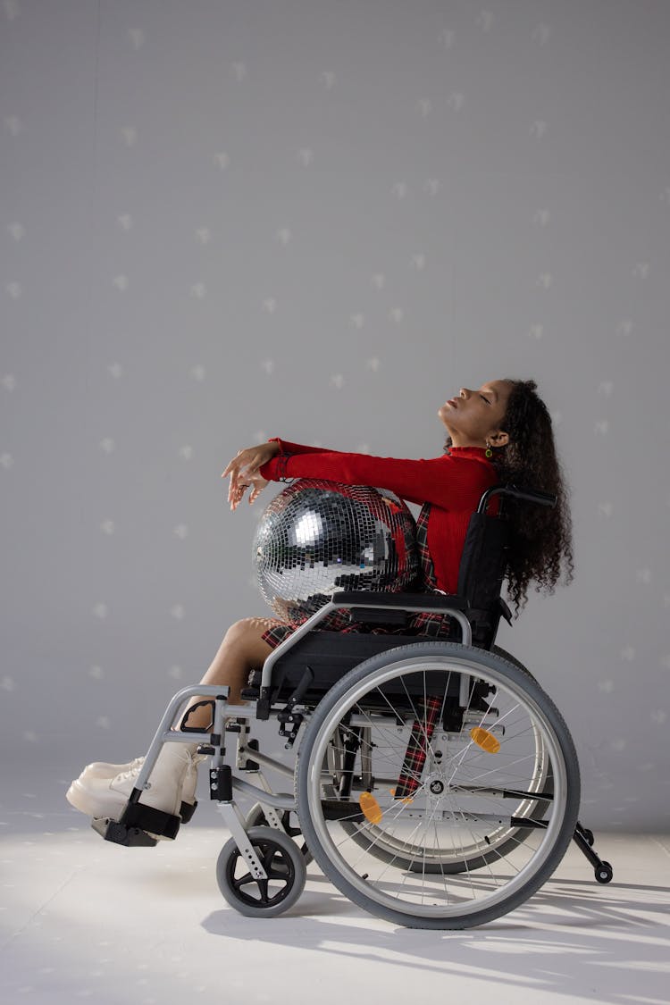 A Young Woman In A Wheelchair Holding A Disco Ball