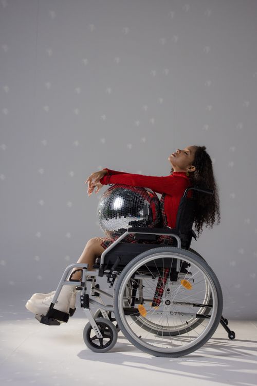 Free Stylish young woman posing with disco ball in wheelchair, studio setting. Stock Photo