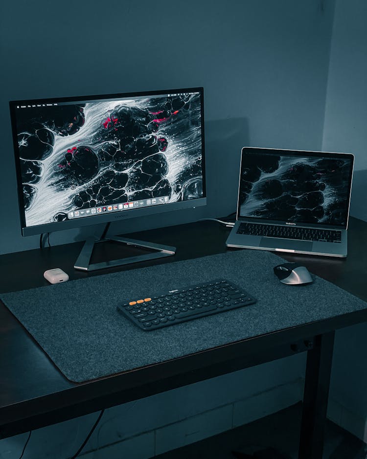 A PC And Laptop Setup On A Computer Table