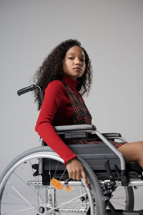 Free Fashionable young woman with elegant attire sitting confidently in a wheelchair in studio. Stock Photo