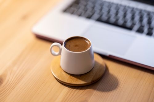 Free A minimalist setup featuring a coffee mug on a coaster beside a laptop on a wooden table. Stock Photo