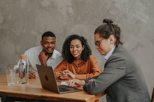 A group of colleagues working together on a laptop in a stylish office setting.
