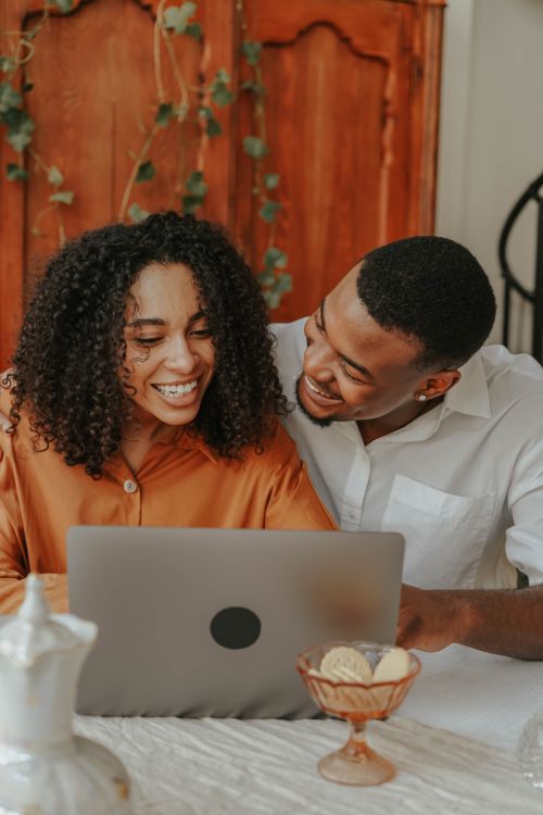Free Smiling couple enjoying online shopping together at home, using a laptop with a warm ambiance. Stock Photo