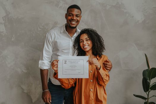 A joyful couple posing with their child adoption certificate indoors.