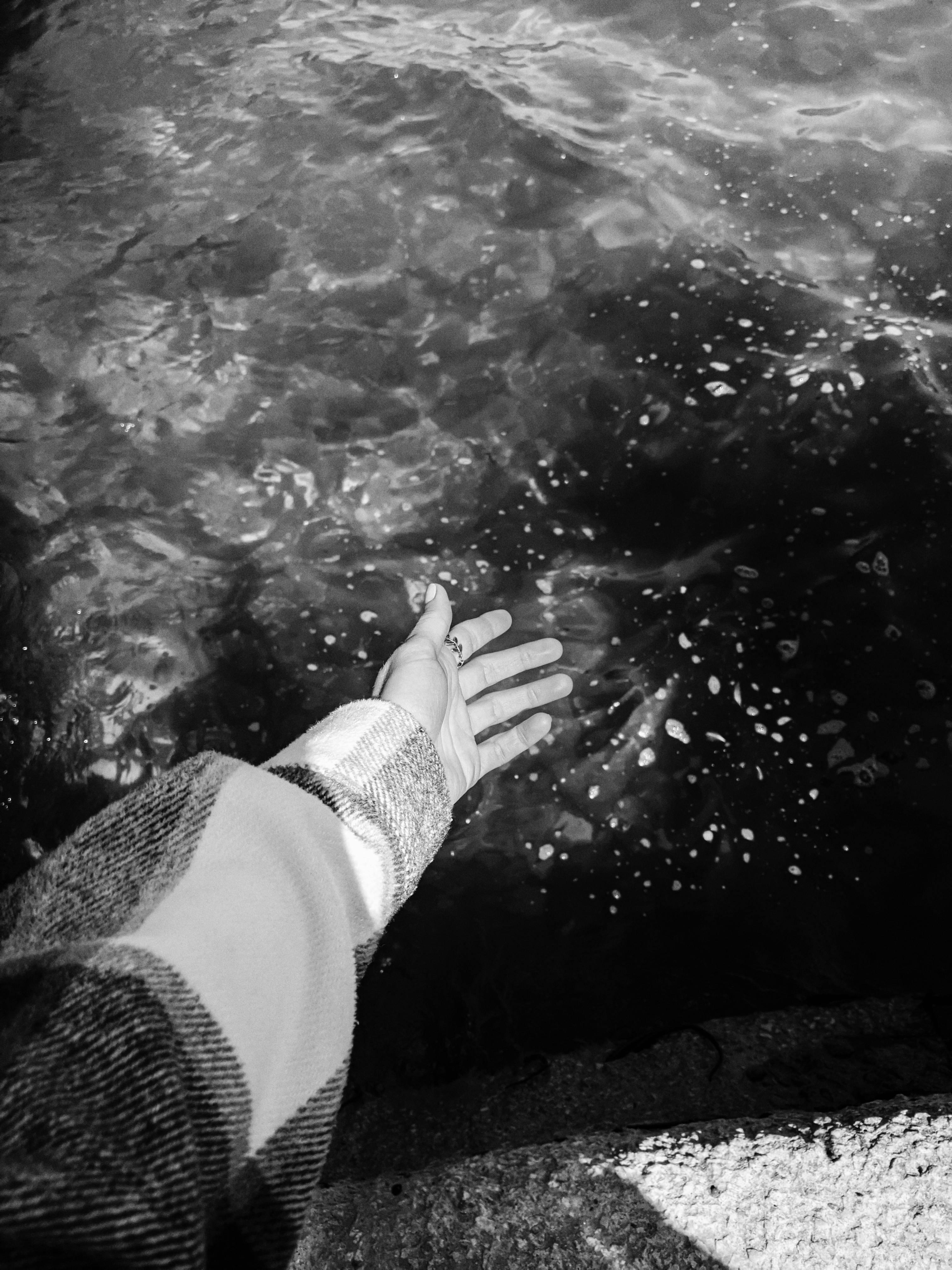 A hand reaches towards the rippling water in a monochrome setting, evoking a sense of serenity.