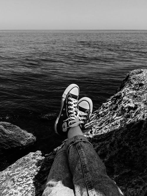 Free Low Section of Person in Black Sneakers and Denim Pants Sitting on a Rock Cliff Stock Photo