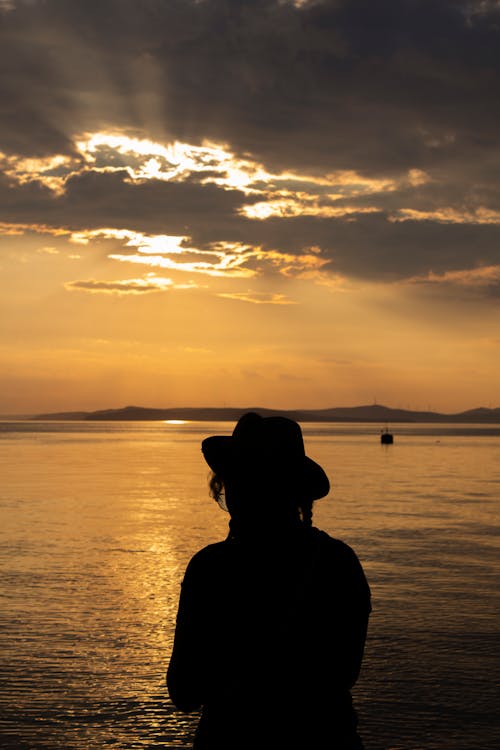 Silhouette of Person Standing Near Body of Water during Sunset