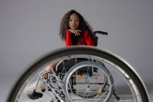 Free A young woman with stylish afro hair confidently sitting in a wheelchair in a studio setting. Stock Photo