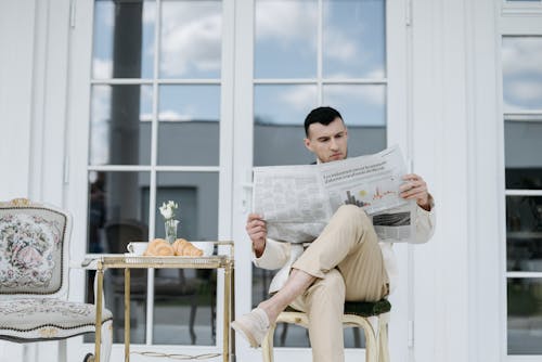 Man in Beige Suit Sitting on a Chair Reading Newspaper