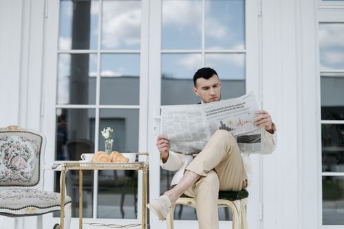 Free A man reading a newspaper outdoors with croissants on a table. Relaxing scene. Stock Photo
