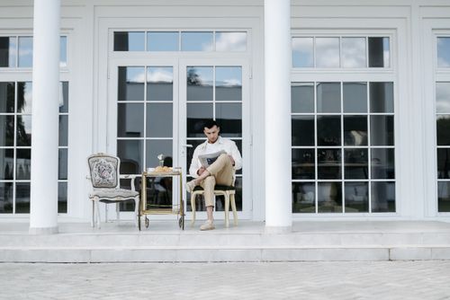 Free Man sitting on a porch reading a newspaper, enjoying leisure time with a cart beside him. Stock Photo