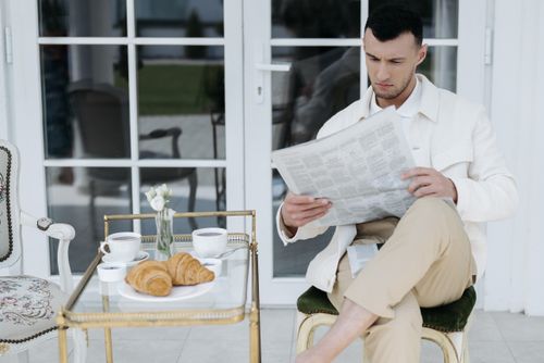 Free Man enjoying morning coffee and croissants while reading a newspaper. Stock Photo