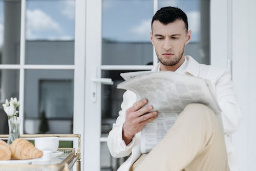 A Man in White Long Sleeves Reading Newspaper