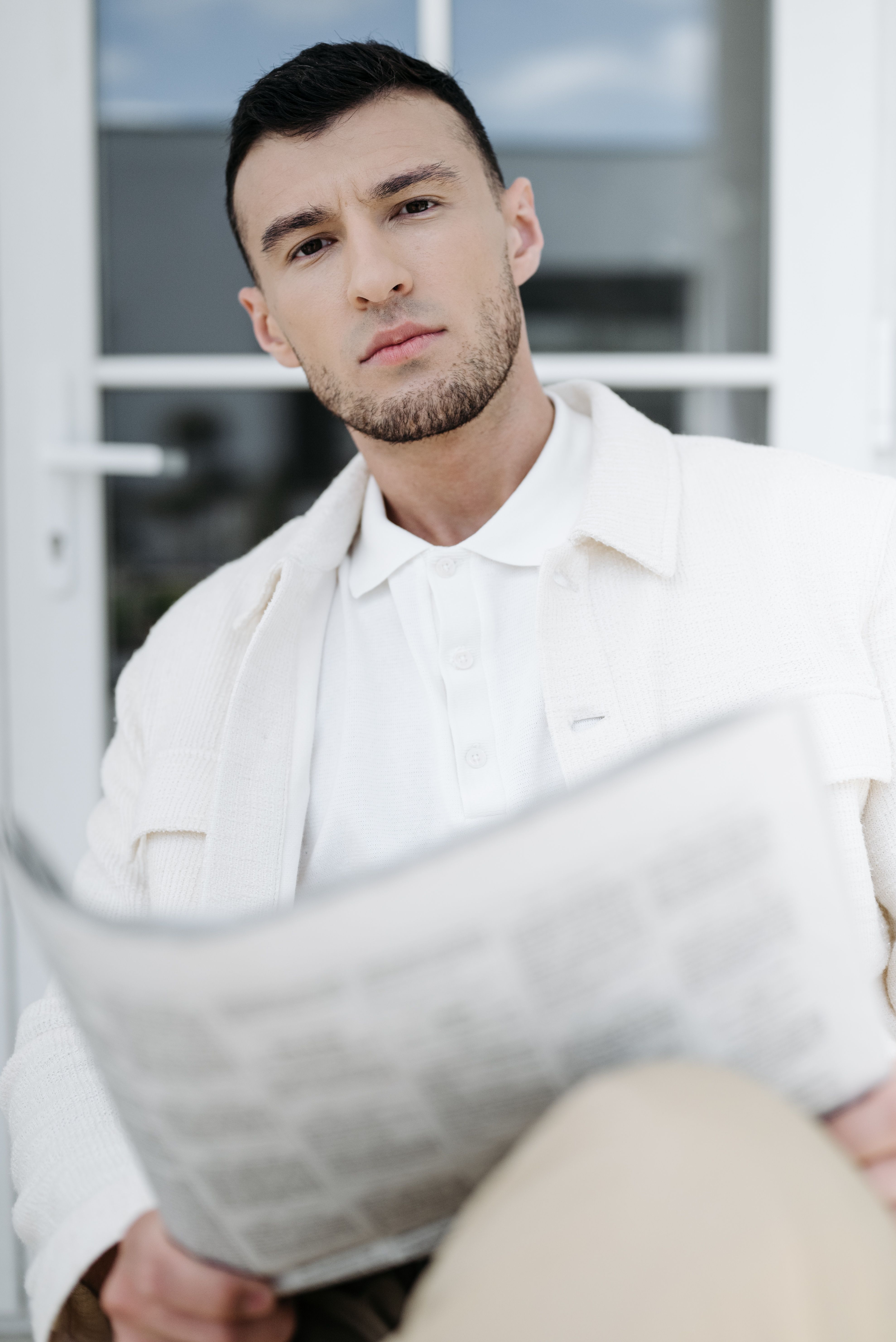 Young man reading a newspaper while relaxing outdoors, dressed in casual attire.