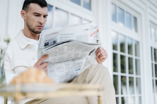 A Handsome Man in White Long Sleeves Reading a Newspaper