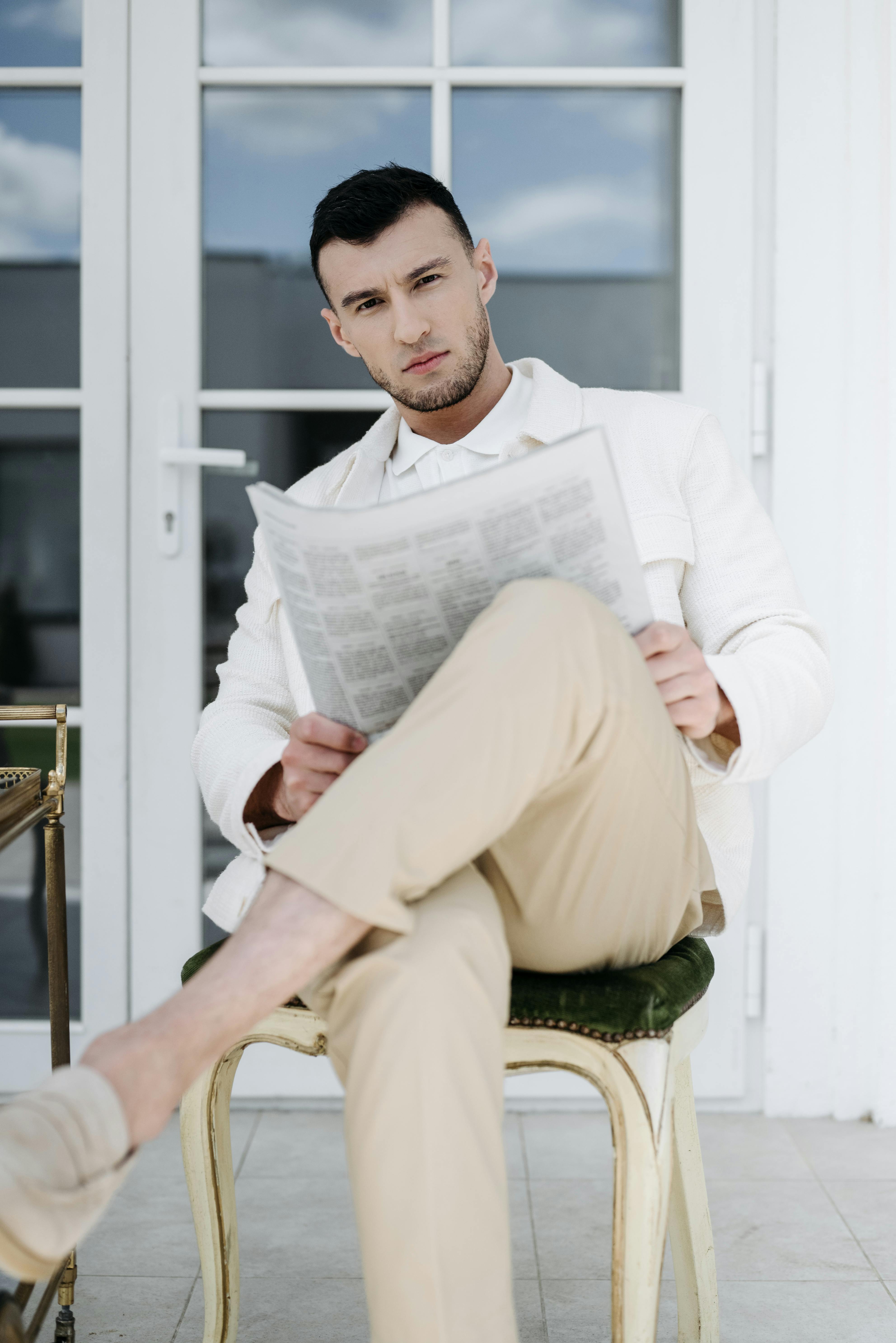 a handsome man in white long sleeves holding a newspaper while sitting