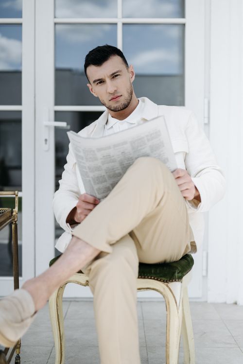 Free Man in beige trousers and white jacket reading a newspaper on a sunny day. Stock Photo