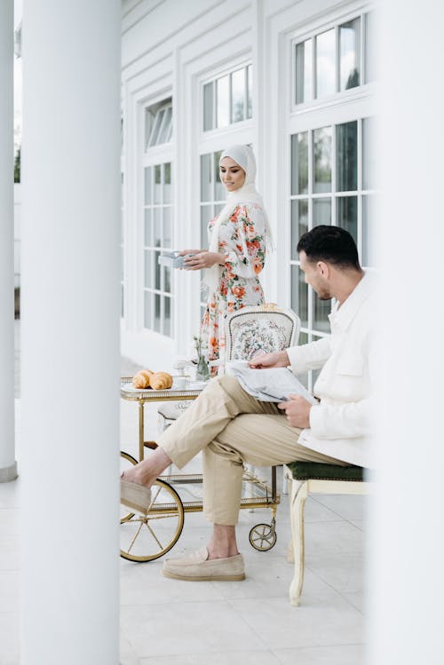 A Woman in Floral Dress Looking at the Man Sitting on the Chair