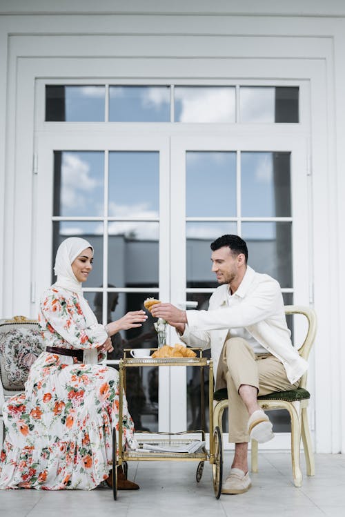 Free Man in White Dress Shirt and Woman in Floral Maxi Dress Sitting in the Patio Having Breakfast Stock Photo