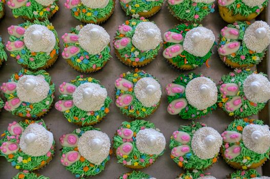 A tray of colorful Easter bunny-themed cupcakes with vibrant icing decorations and sprinkles.