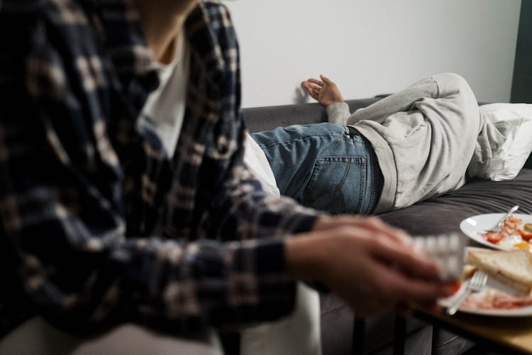 A Person In Gray Jacket Lying On The Couch Beside The Table With Leftover Food