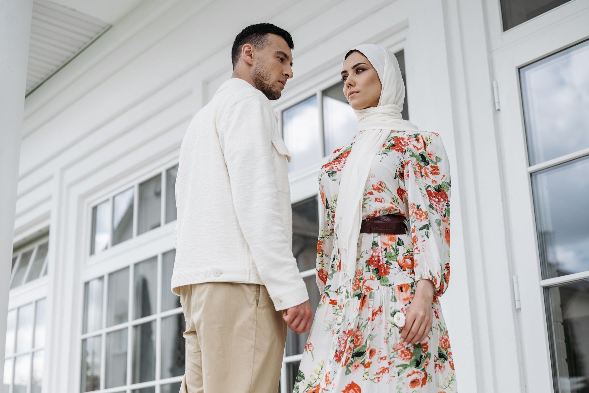A fashionable couple holding hands in front of elegant French doors, exuding contemporary style.