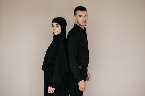 Free Back-to-back studio portrait of a couple in black attire, featuring a hijab. Stock Photo