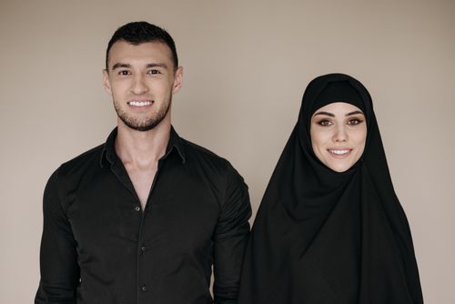 Free A studio portrait of a smiling Muslim couple in black clothing, showcasing cultural attire with a modern touch. Stock Photo