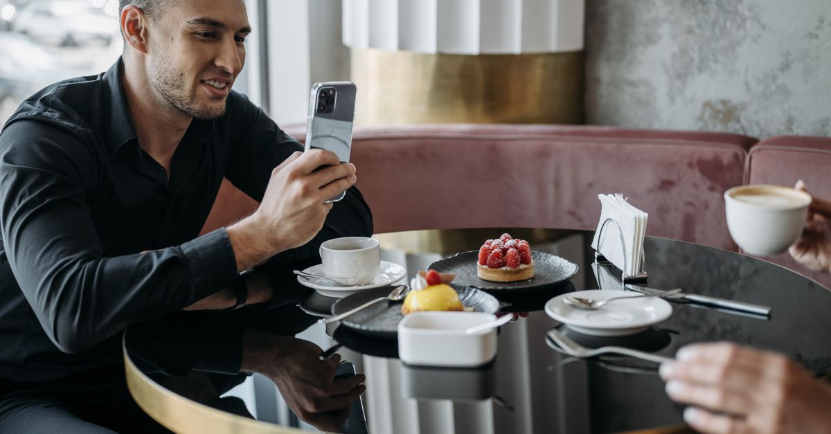 A man taking a photo of desserts at a modern café table while enjoying a coffee.