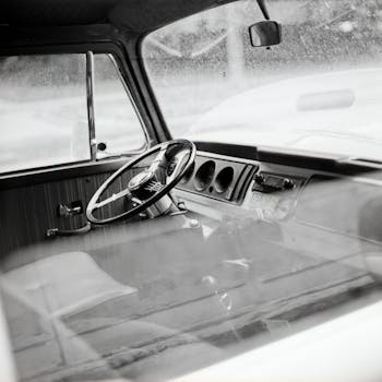Black and white photo of vintage car interior showcasing steering wheel and dashboard.