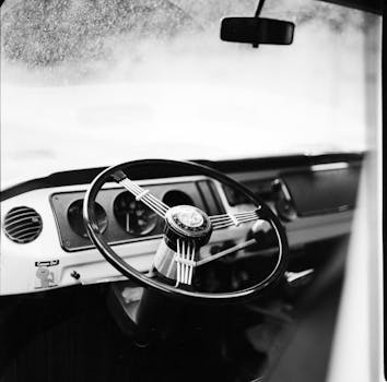 Close-up view of a vintage car's interior featuring a classic steering wheel and dashboard in monochrome.