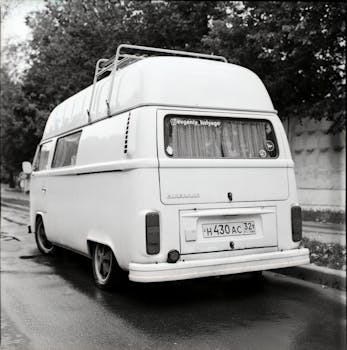 A classic campervan parked on a wet street, captured in monochrome.