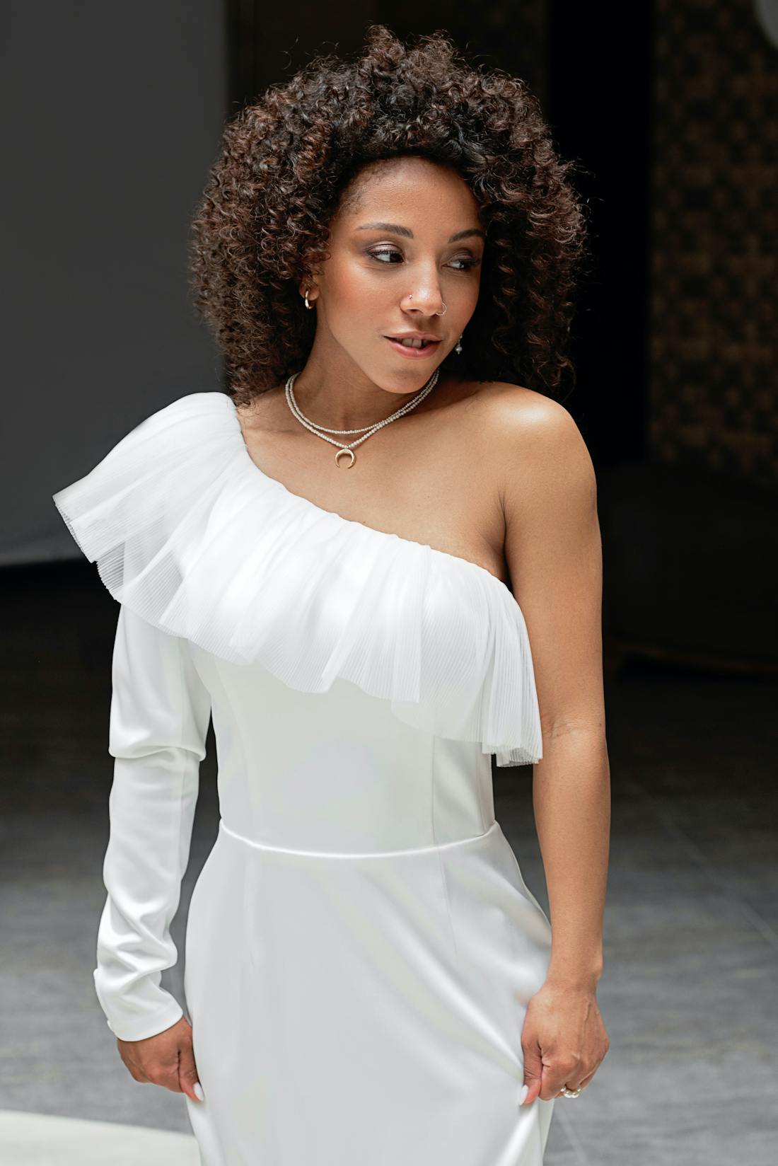 One-shoulder white gown with ruffled sleeve and flowing trail