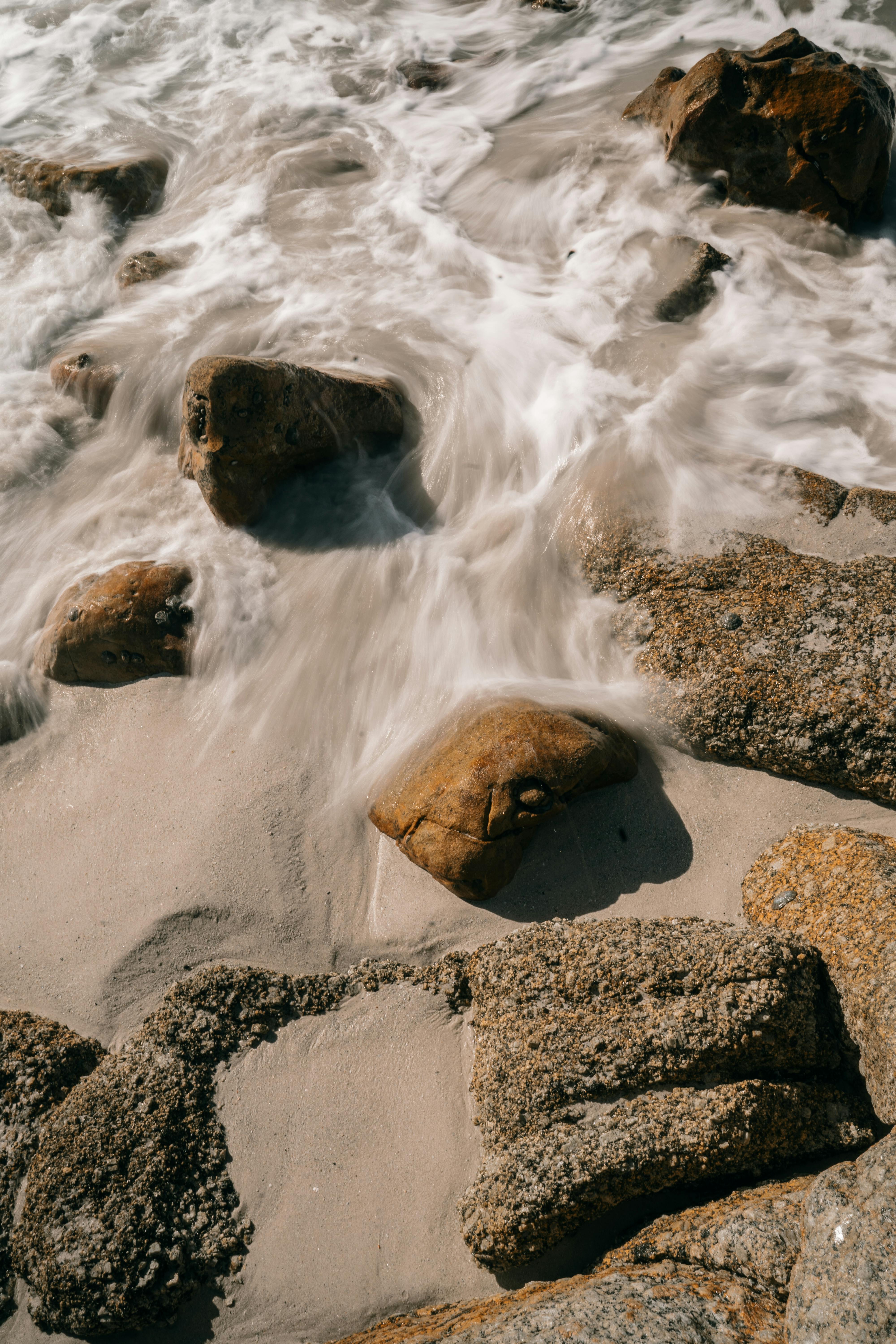 白天，平静的海浪轻轻地冲刷着宁静的沙滩上的岩石