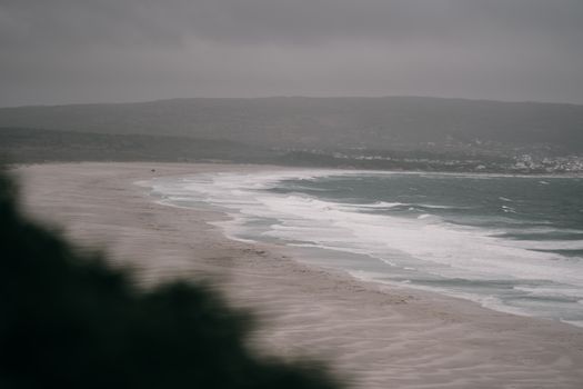 Expansive beach with crashing waves under overcast skies. Ideal for nature enthusiasts.
