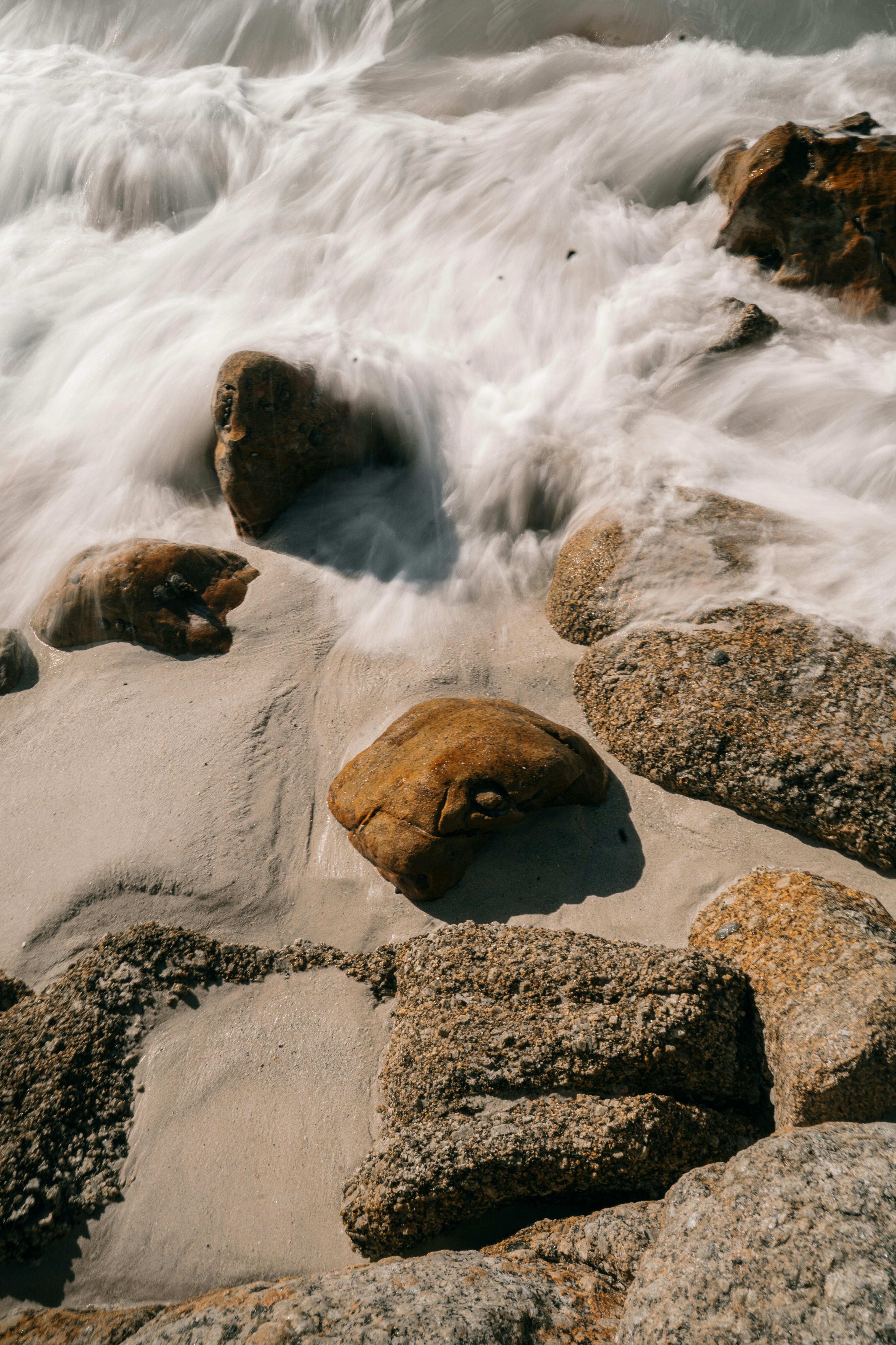 长时间曝光海浪流过沙滩上纹理丰富的岩石，捕捉宁静的动感和自然之美