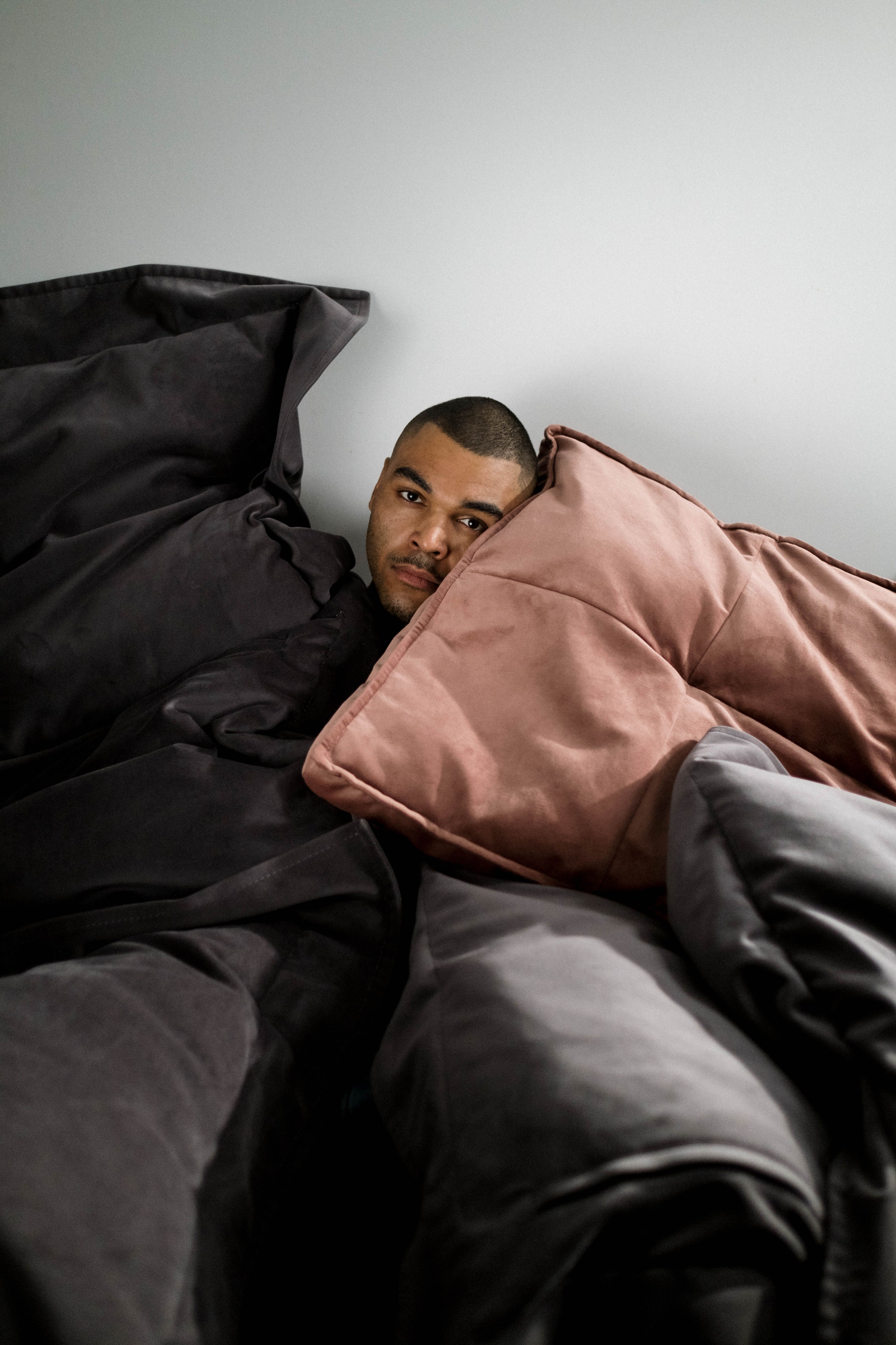 Man resting surrounded by dark and muted pillows, reflecting a contemplative mood.