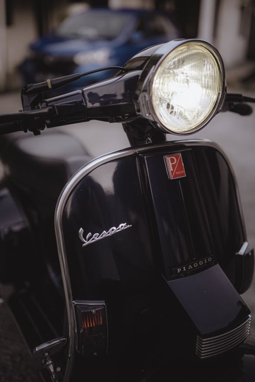 Free Close-up of a classic Vespa scooter with its headlight illuminated, showcasing vintage design. Stock Photo
