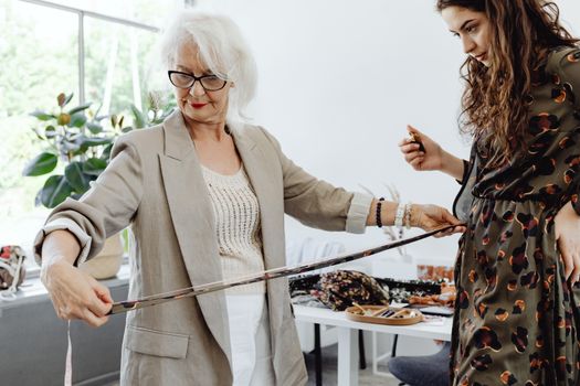 Elderly woman measuring a young woman's waist with tape in a comfortable indoor setting.