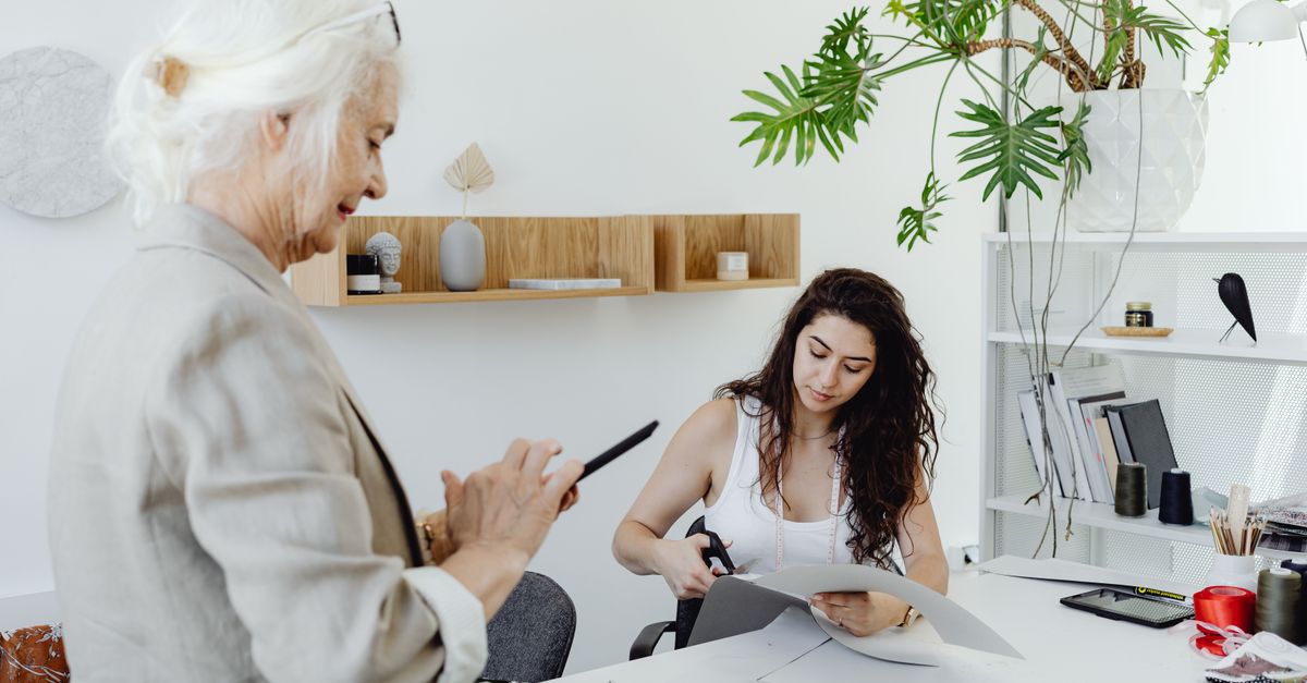 Duas mulheres colaborando em um estúdio de design moderno com tecidos e decoração de escritório.