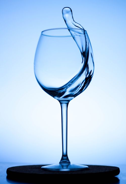 Free A captivating splash of water inside a wine glass against a blue background. Stock Photo