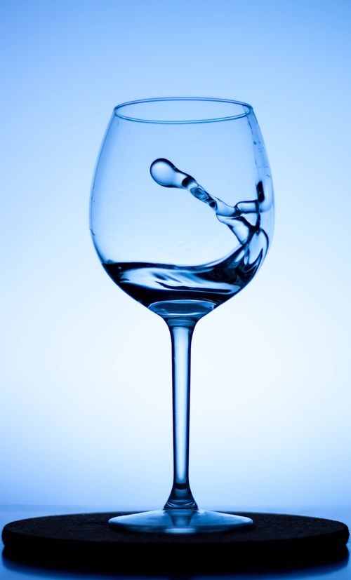 Free A dynamic splash captured in a wine glass filled with water, highlighting fluid motion. Stock Photo