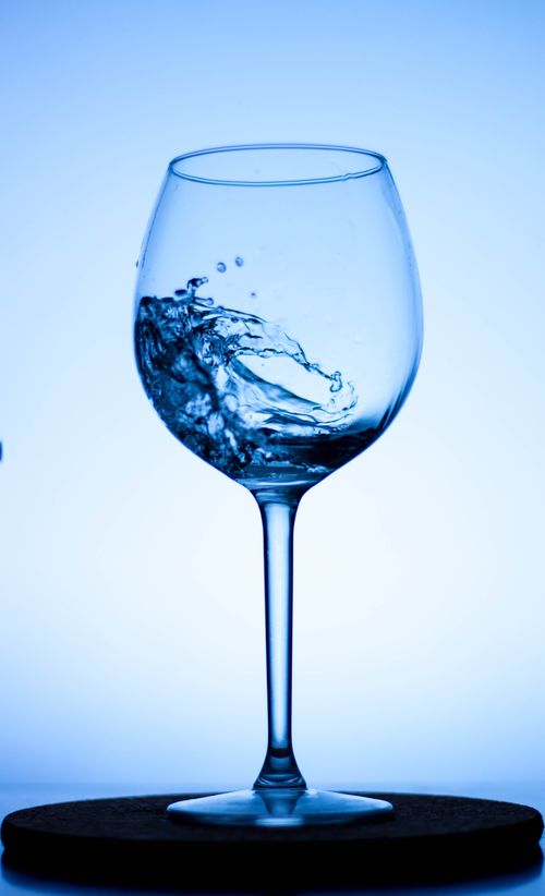Free Close-up of water splashing inside a wine glass against a clean, blue background. Stock Photo