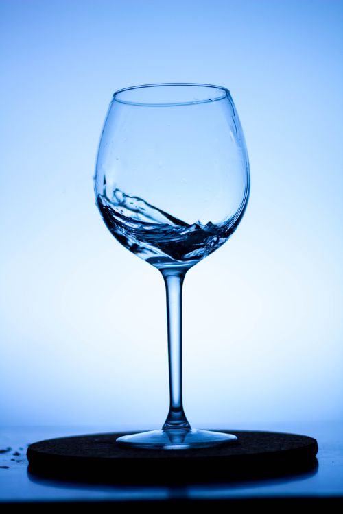 Free Close-up of a wine glass with water swirling elegantly against a blue background. Stock Photo