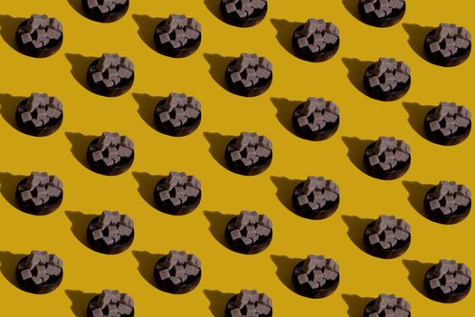 Abstract display of brown sugar cube piles on yellow background, forming a seamless pattern.