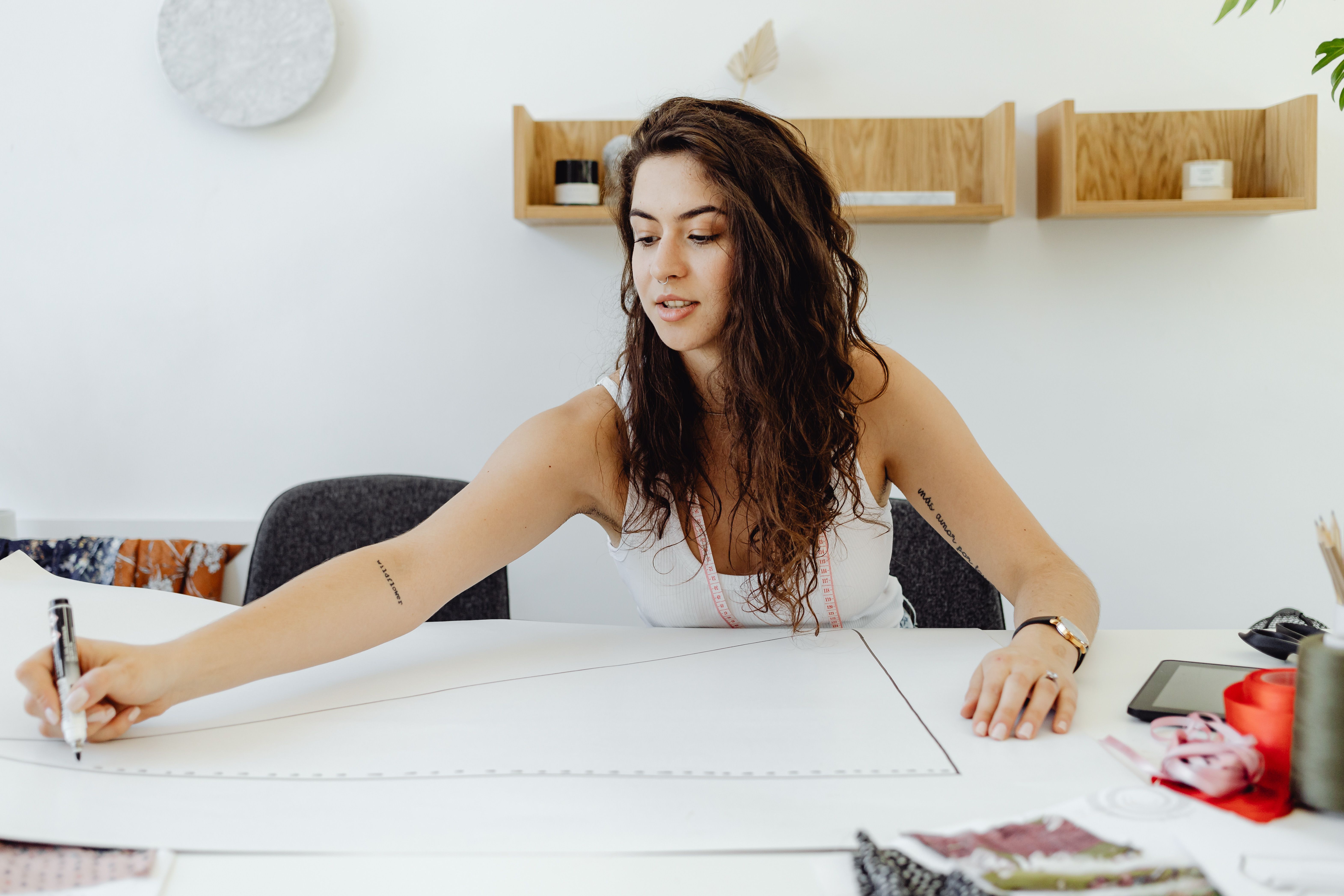 A young woman seamstress carefully designs fashion patterns indoors at a modern workspace.