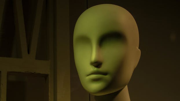 A striking green mannequin head sculpture with a smooth, faceless surface set against a dark backdrop.